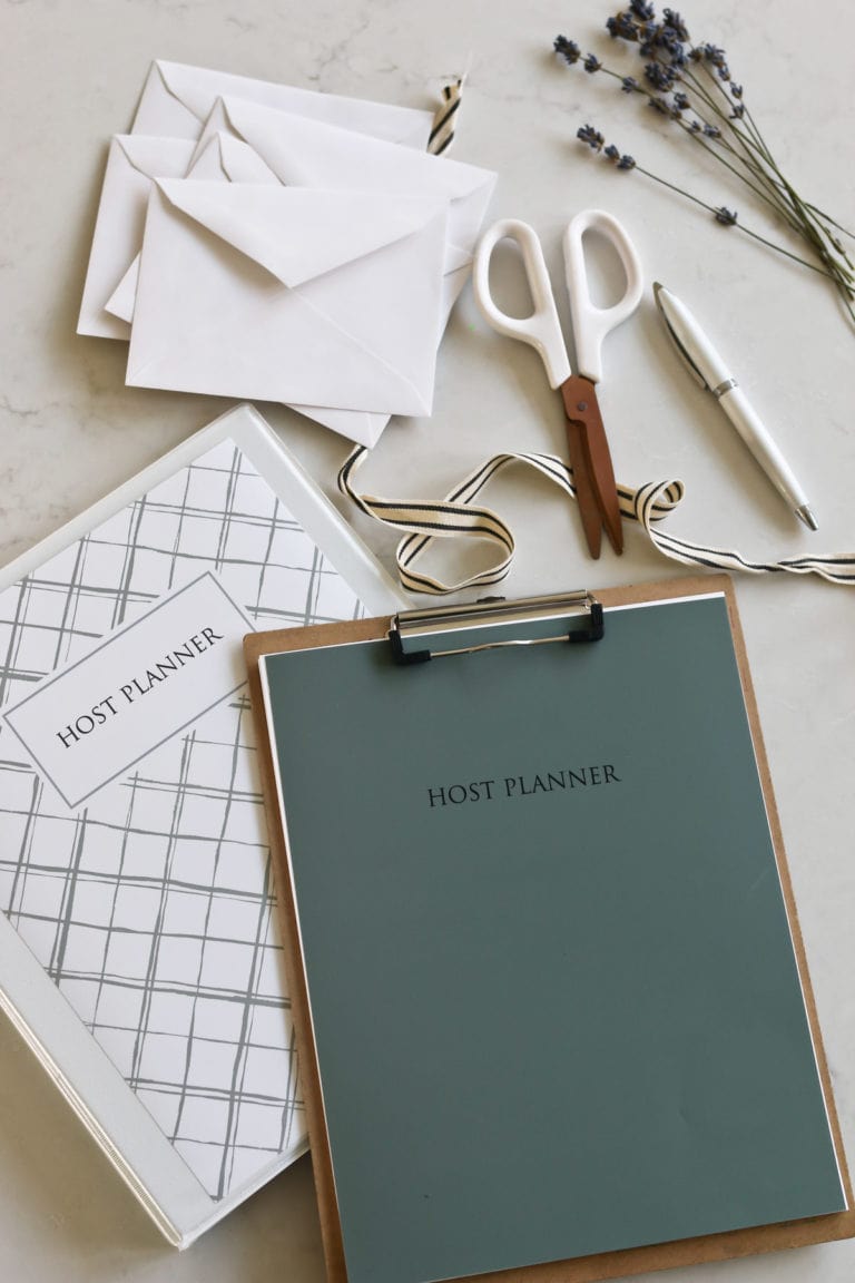 The Host Planner binder placed next to scissors, ribbon, a pen, and envelopes