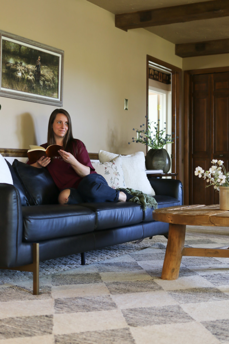 A woman sits on a black leather sofa while reading a book