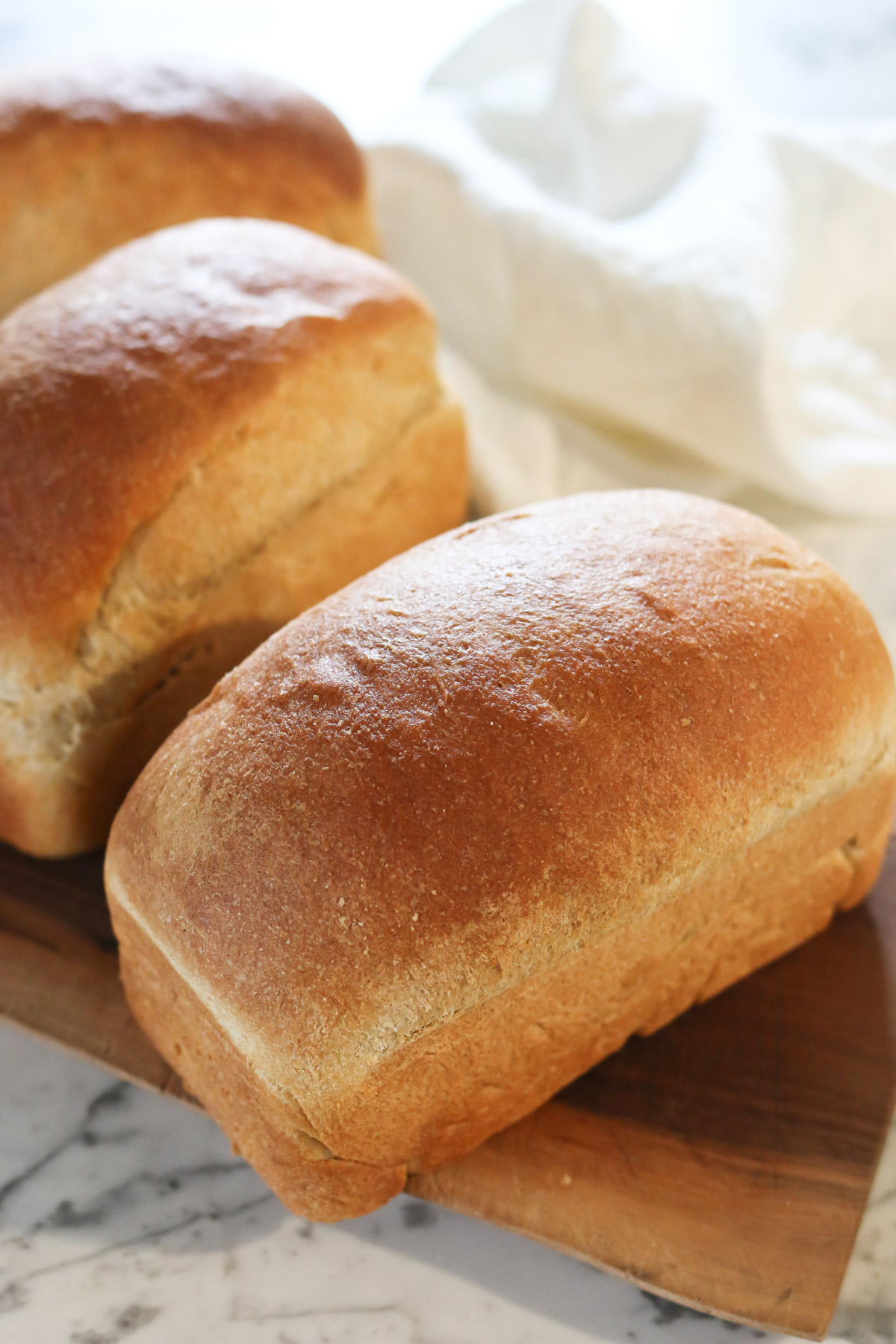 3 loaves of freshly baked homemade bread sit on a cutting board