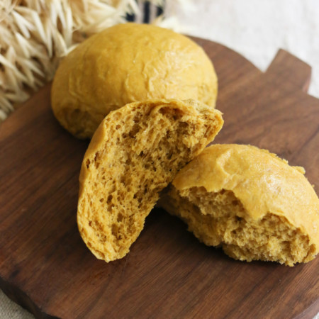 Moist and fluffy pumpkin dinner rolls made with whole wheat flour rest on a wooden cutting board