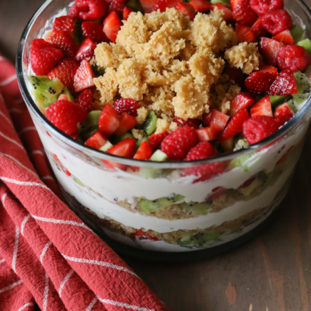 A glass serving bowl holds a layered trifle cake made with fruit, whipped cream and whole wheat cake