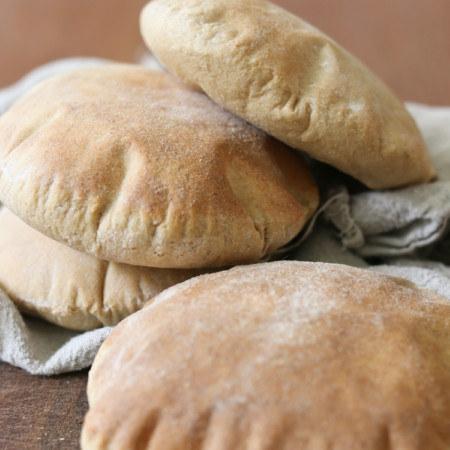 Several puffy homemade pita pockets are stacked together on a table