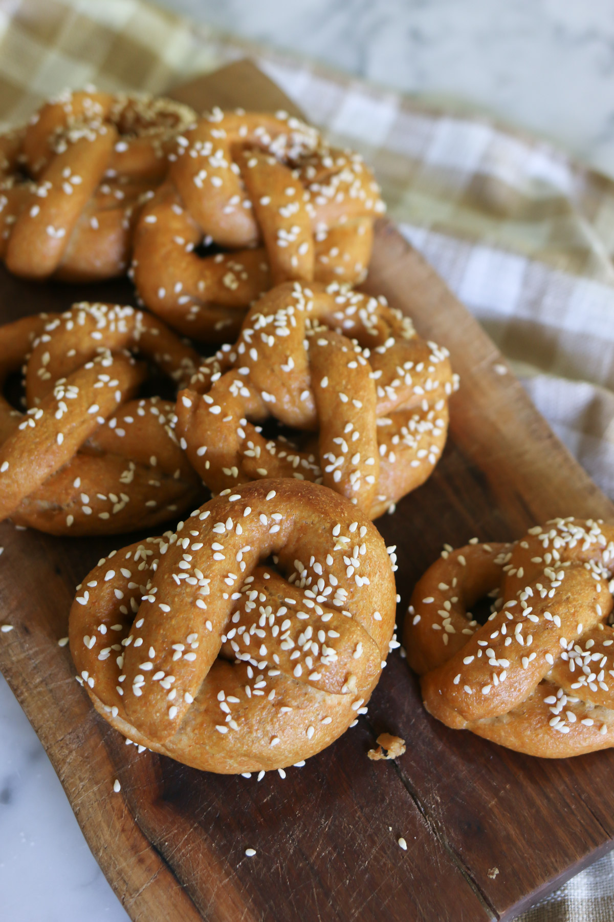 A handful of soft, homemade pretzels topped with sesame seeds sit on a wooden cutting board