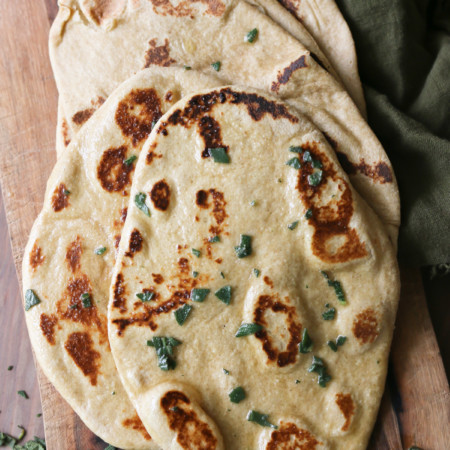 A pile of naan bread has been sprinkled with herbs and oil after baking