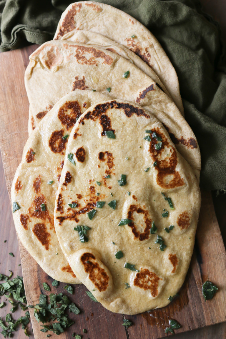 A pile of naan bread has been sprinkled with herbs and oil after baking