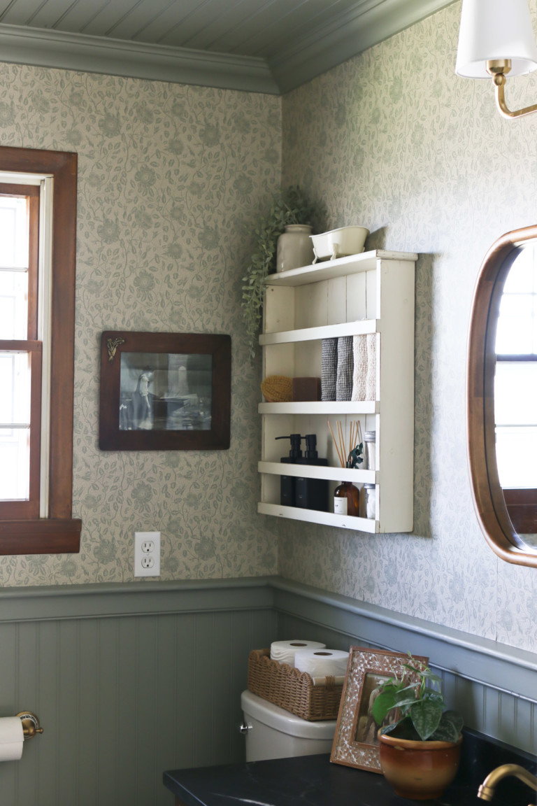 A white shelf hangs on a bathroom wall above the toilet and next to a framed mirror