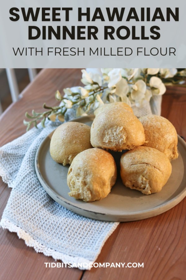A plate holds several Hawaiian sweet dinner rolls along side a tea towel and white flowers
