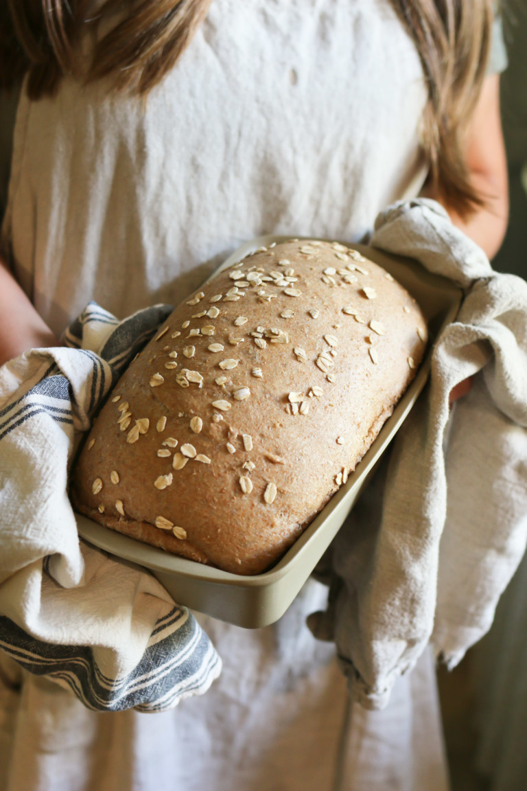 A loaf of freshly baked bread still in a bread pan is held by a person with a linen cloth
