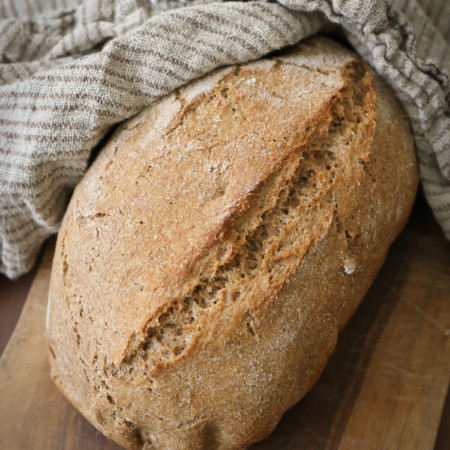 A loaf of rustic artisan bread made with freshly milled flour rests next to a linen tea towel