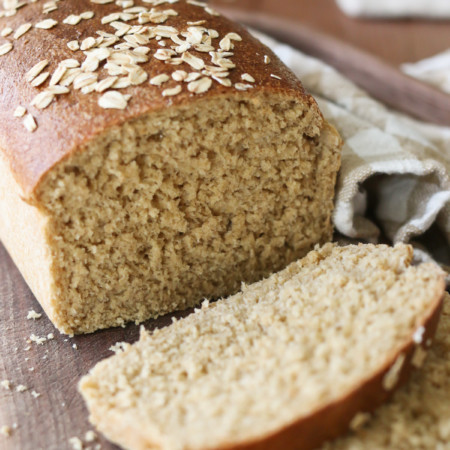 A freshly baked loaf of bread is topped with oats and sliced open to reveal a tender slice of bread