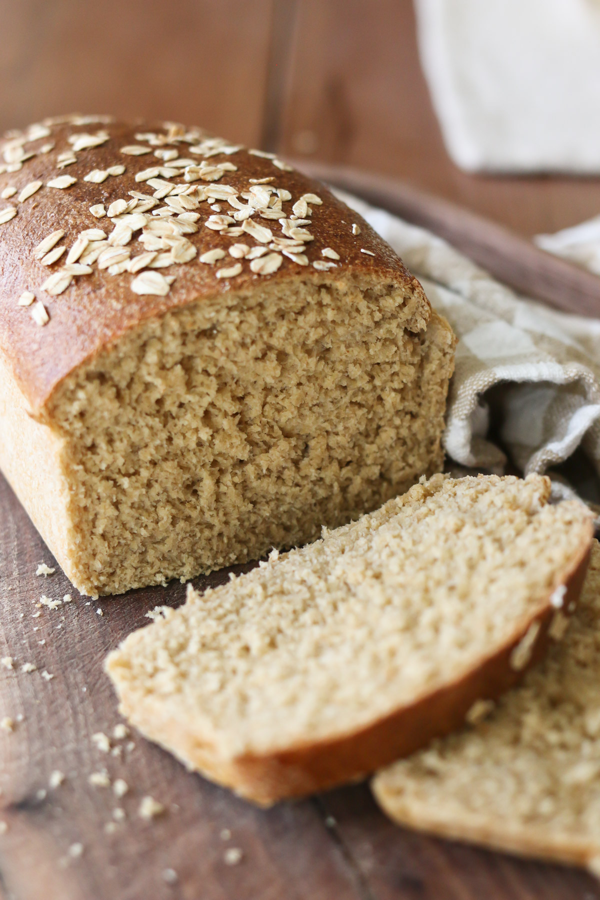 A freshly baked loaf of bread is topped with oats and sliced open to reveal a tender slice of bread