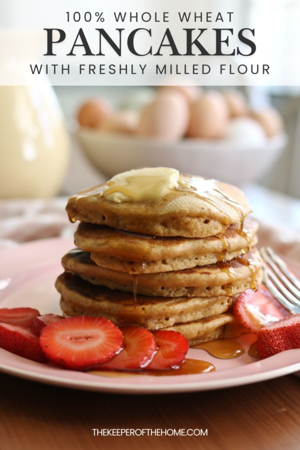 A stack of homemade pancakes made with fresh milled whole grain flour is surrounded by sliced strawberries