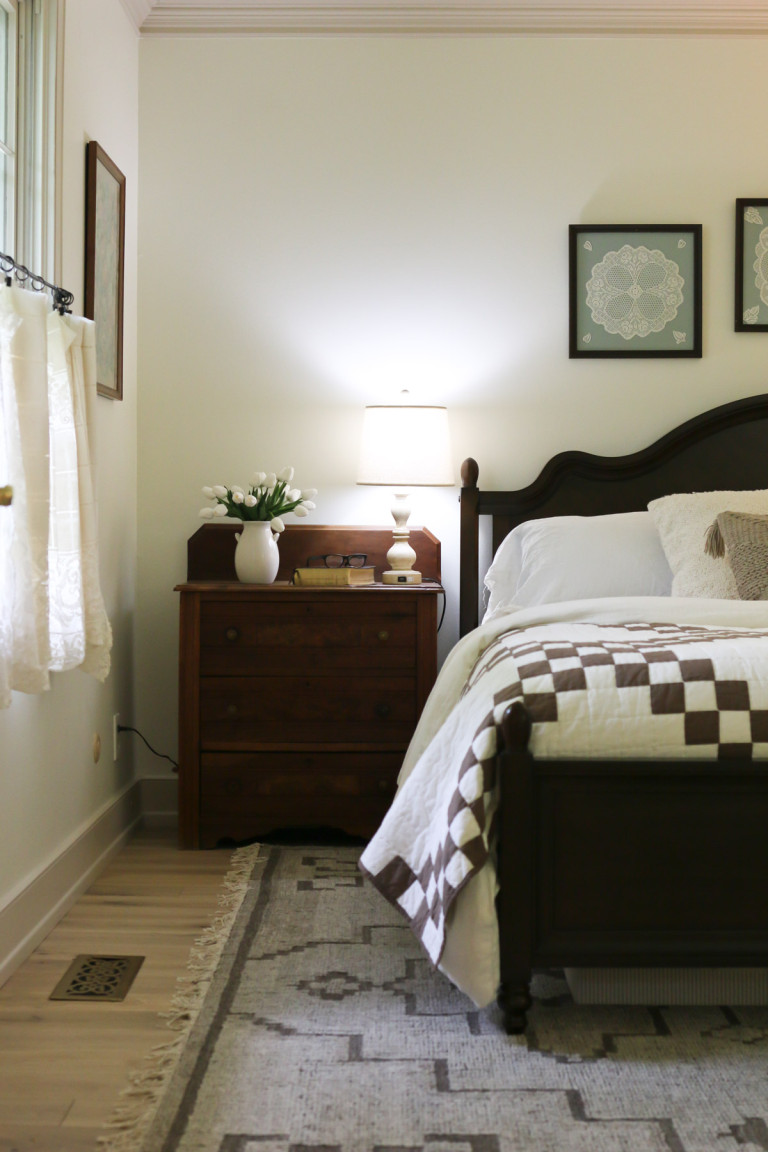 A neutral-colored rug rests beneath a bed and a vintage side table