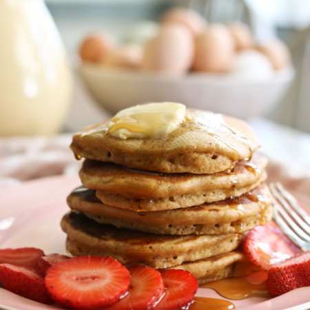 A stack of healthy whole wheat pancakes made with freshly milled flour are stacked and topped with butter and syrup