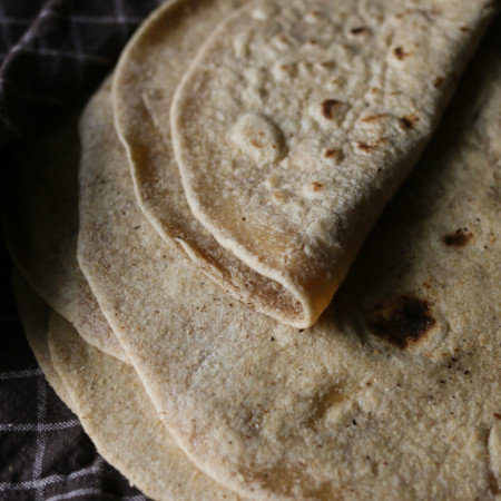 A pile of homemade freshly milled flour tortillas is displayed on a kitchen table
