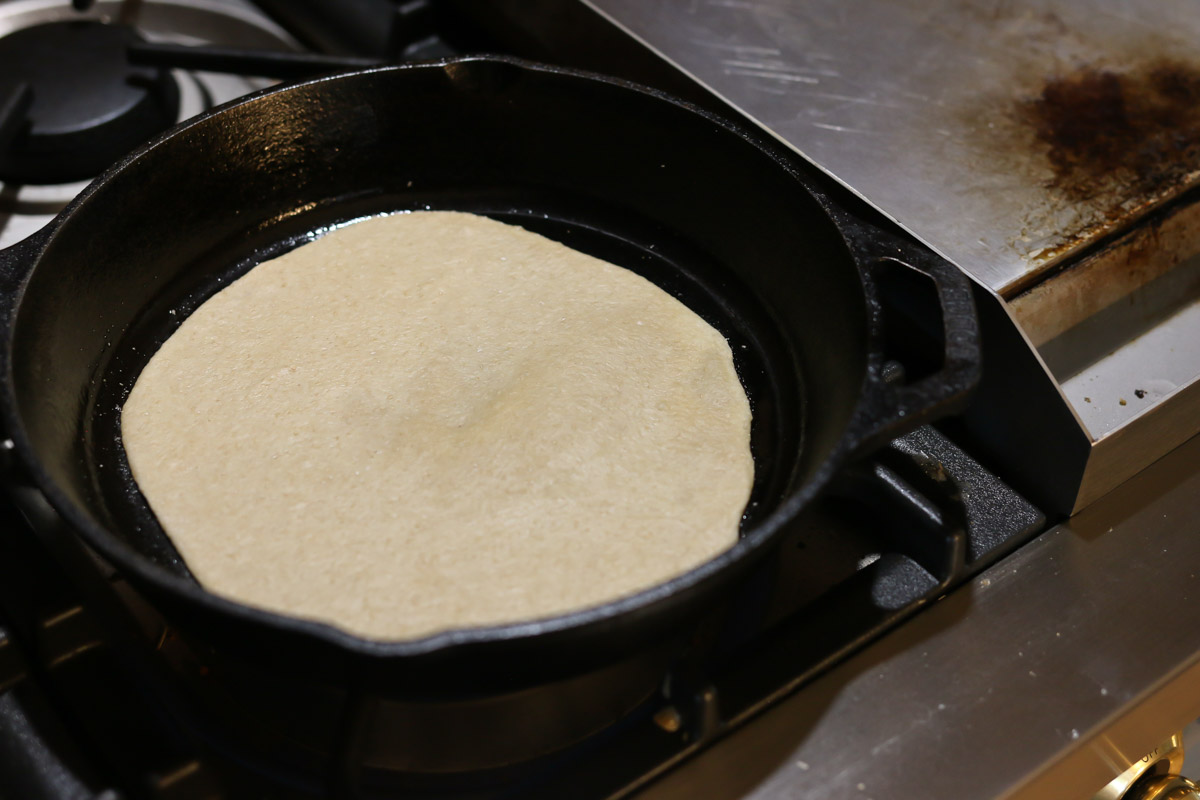 Tortilla dough is cooked in a hot cast iron pan on the stovetop