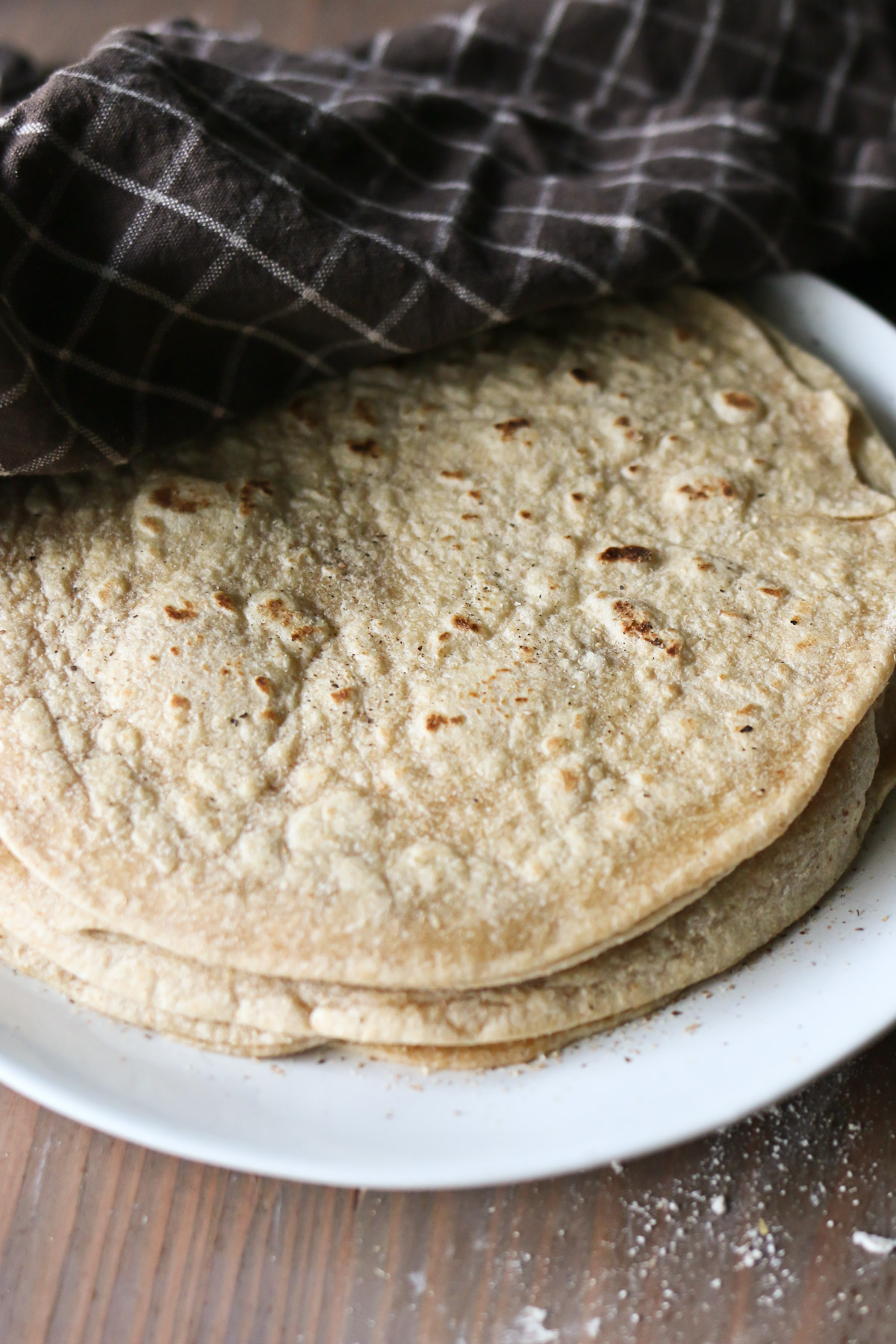 A stack of homemade whole wheat tortillas is piled onto a serving plate