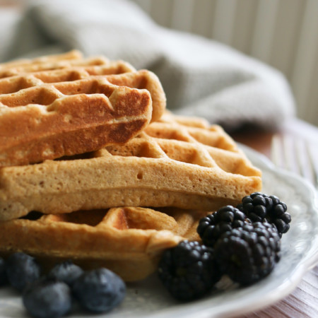 A stack of waffles made with freshly milled whole wheat flour are served alongside blackberries and blueberries