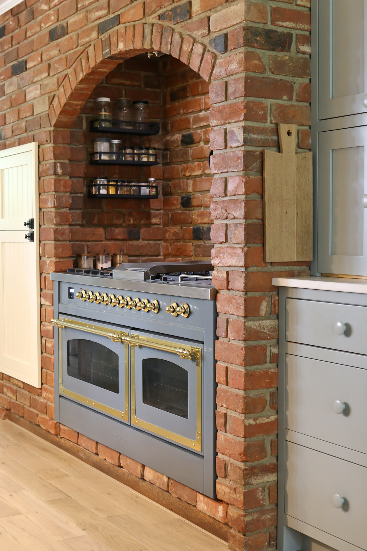 A classic style blue gray kitchen range features double ovens with glass windows and brass hardware