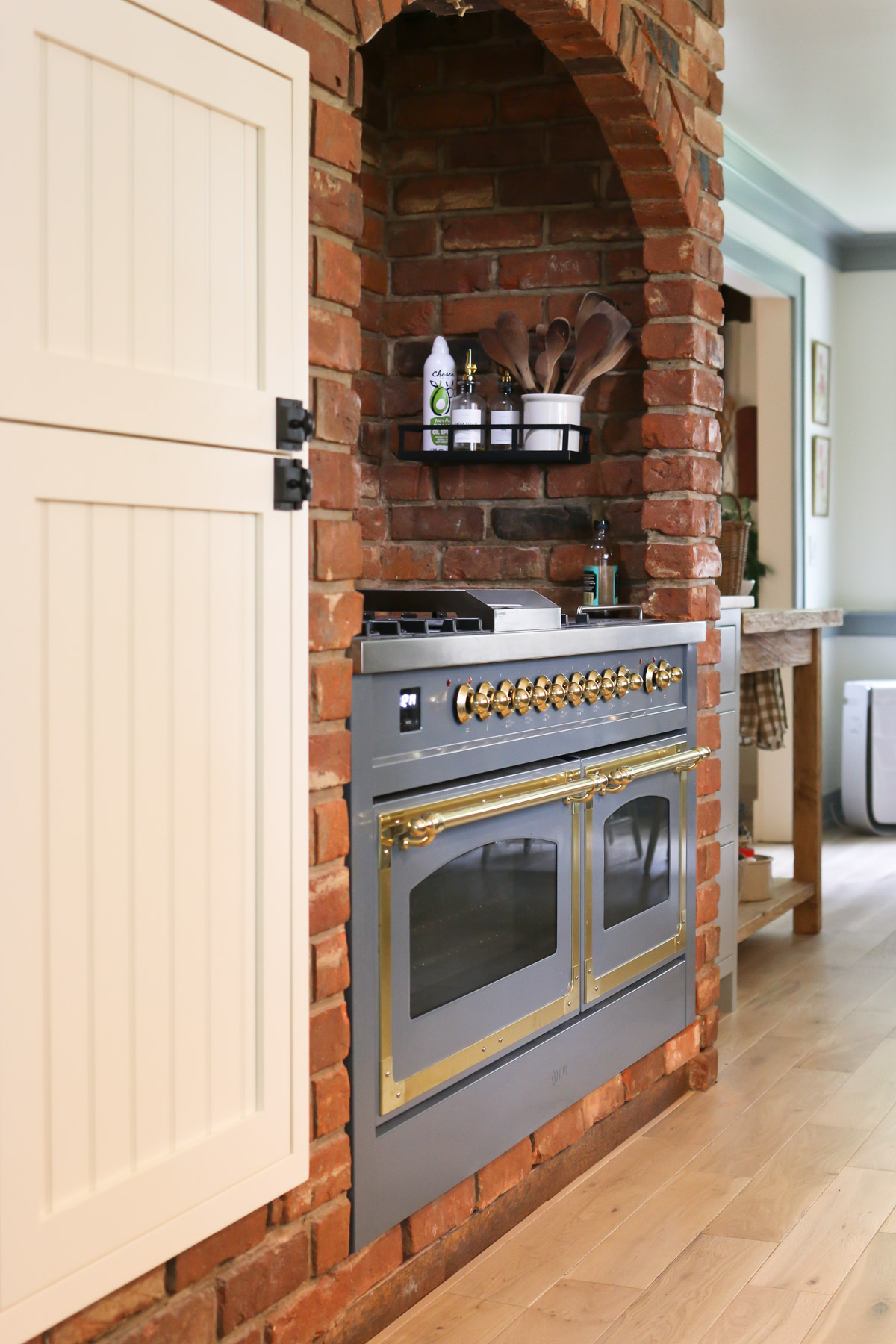A large kitchen range is enclosed with a red brick surround in a cottage style home