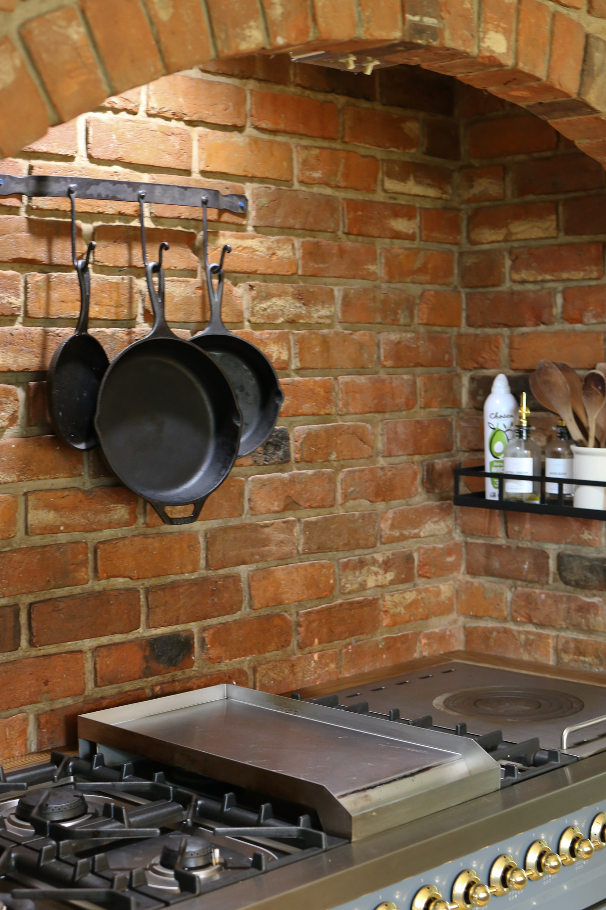 Cast iron pans hand on a brick wall above a fancy Italian kitchen range