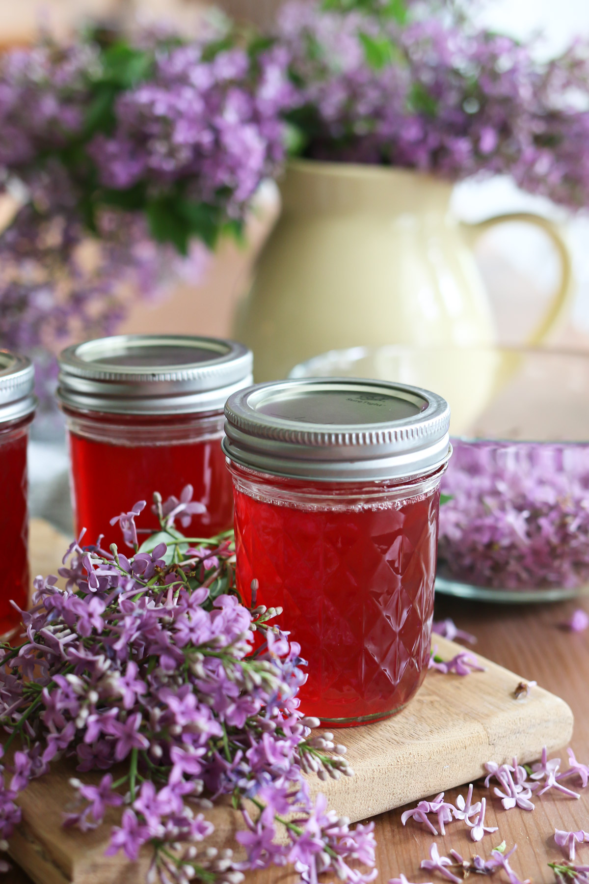 2 mason jars hold lilac jelly that is a vibrant pink color next to some lilac flowers