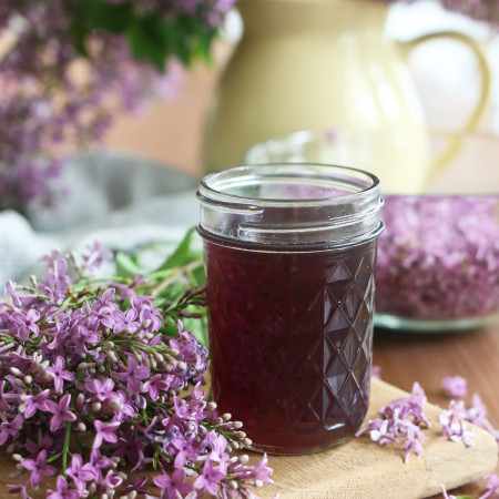 A jar of lilac simple syrup is displayed next to clusters of purple lilac flowers