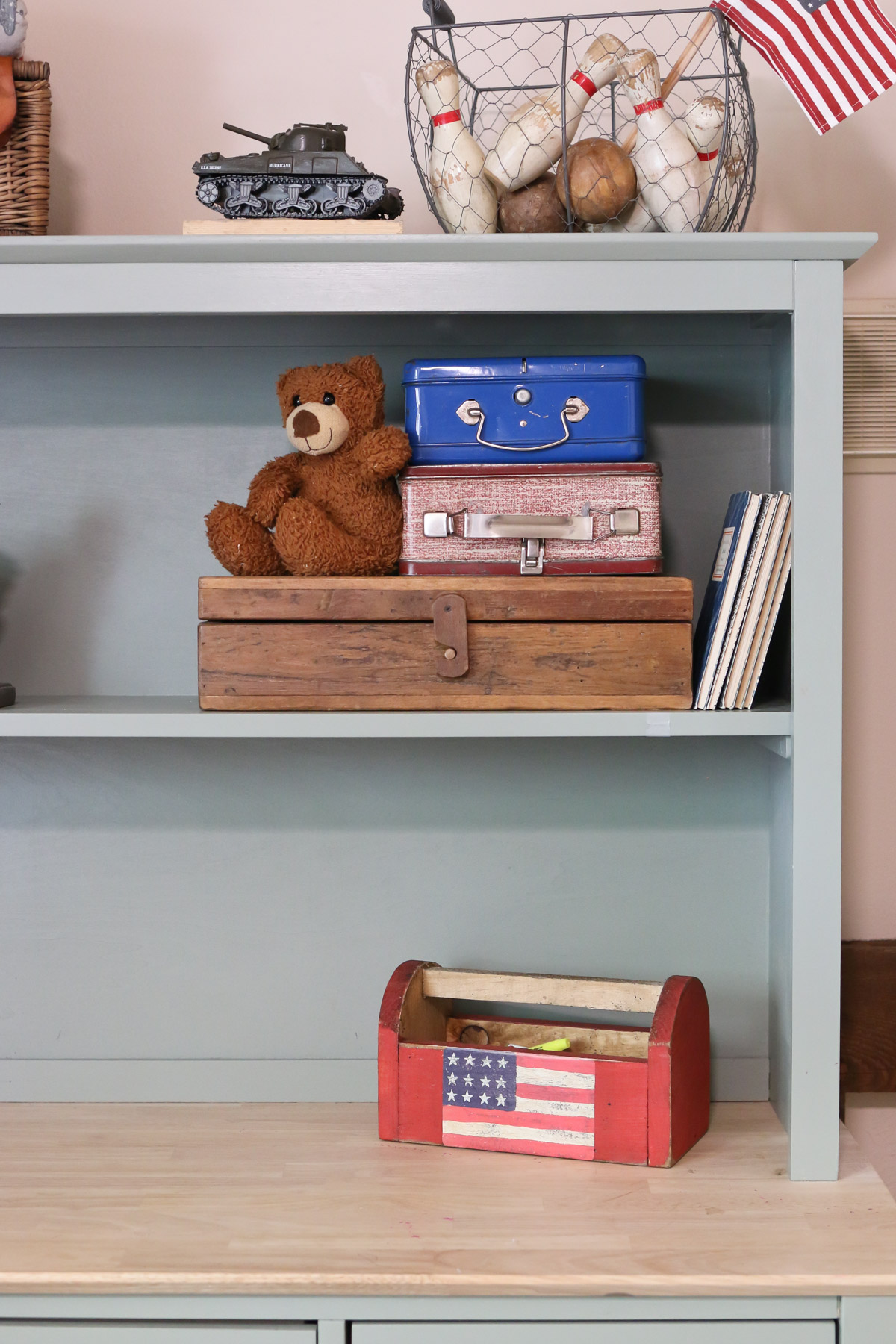 A teddy bear sits next to vintage Americana storage boxes and books on a shelf