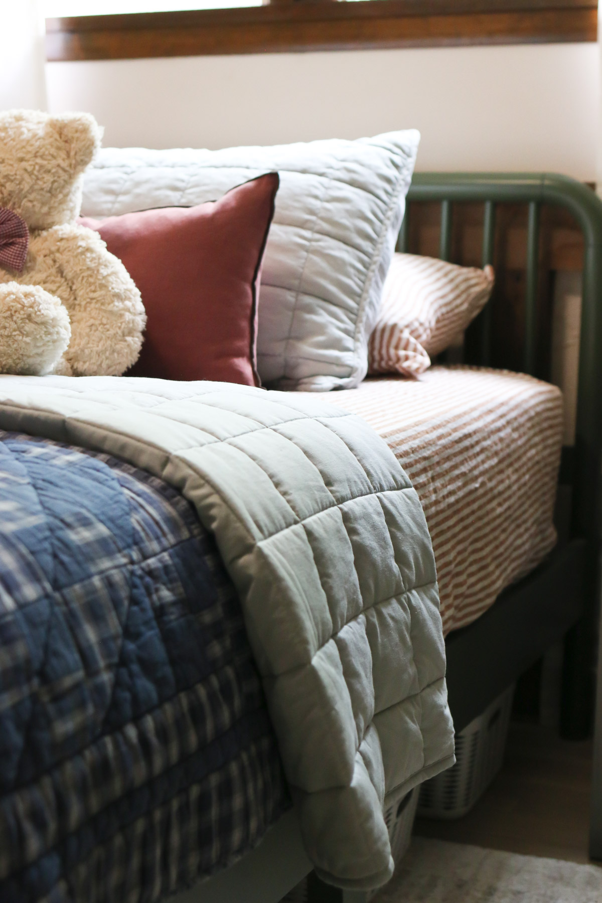 A bed is made with linens in shades of rusty red, blues and whites for an Americana decorating idea theme