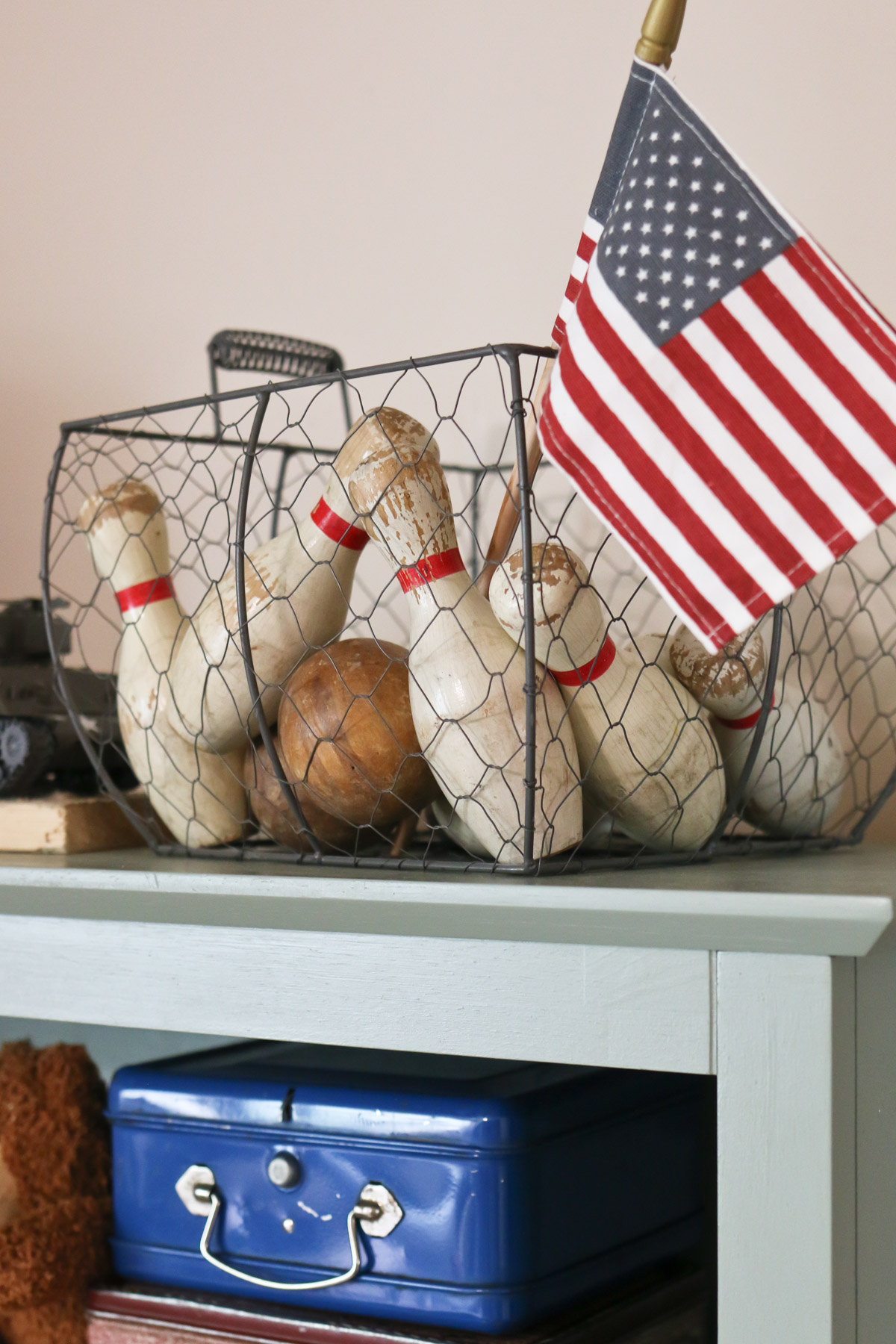 Antique bowling pins and a miniature American flag are displayed in a metal basket as patriotic Americana decor ideas