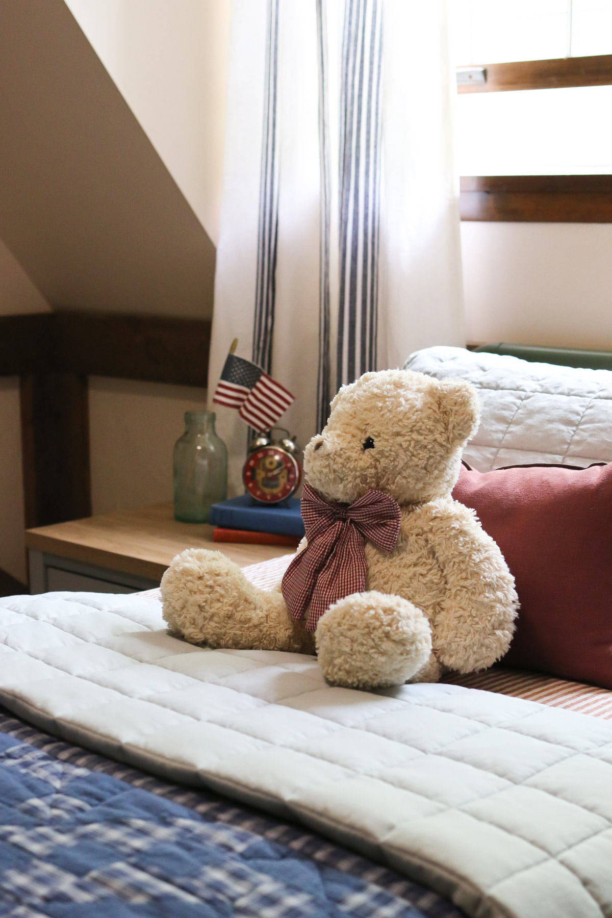 A teddy bear rests on a bed that has been decorated with red, white and blue linens in an Americana style
