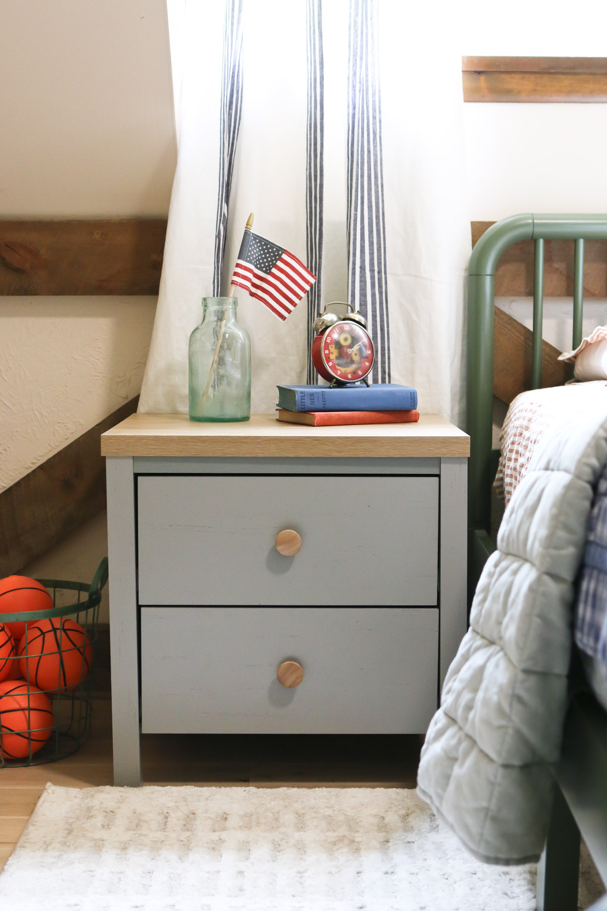 A flag and a clock decorate an end table next to a boys bed