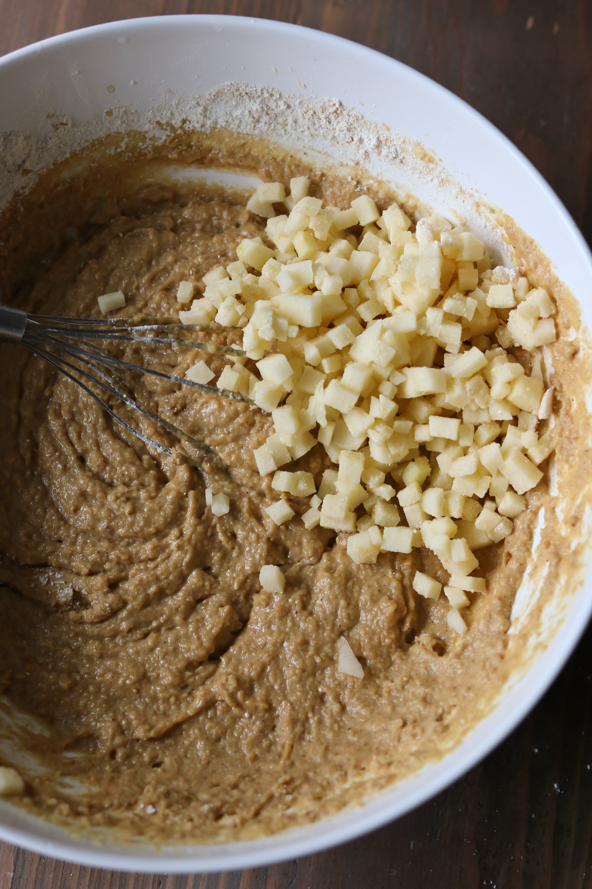 A bowl holds muffin batter and finely diced pieces of apple