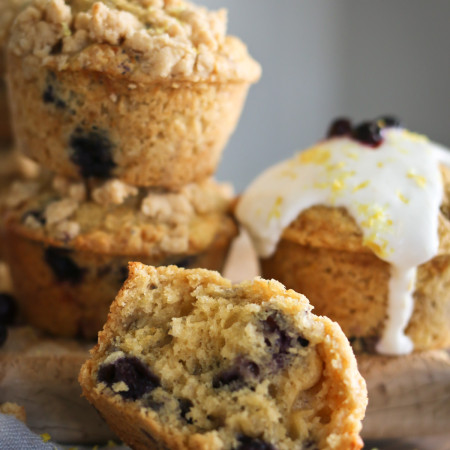 Several blueberry lemon muffins with various toppings are arranged together on a cutting board