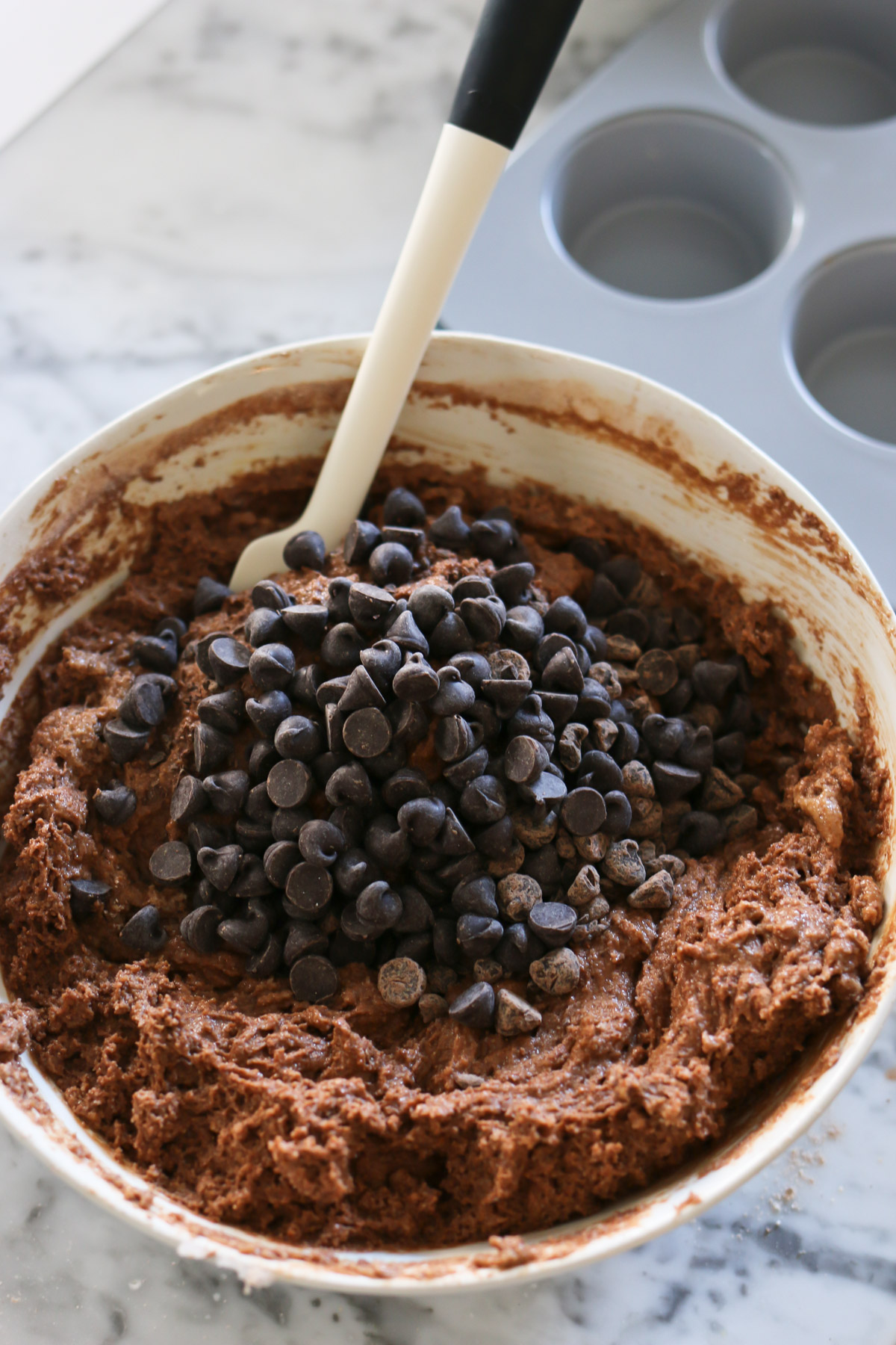 A pile of chocolate chips sit atop a bowl of batter for a healthy chocolate muffin recipe