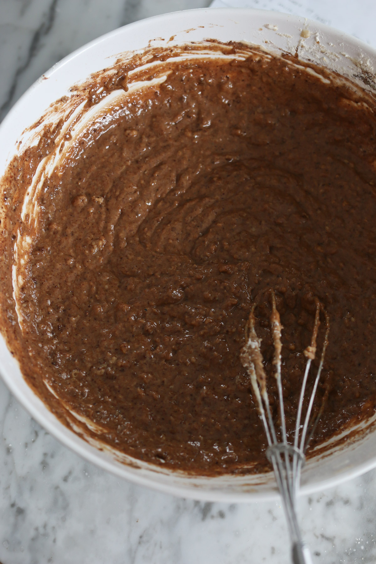 A whisk sits in a bowl of chocolate batter made with healthy whole grain flour