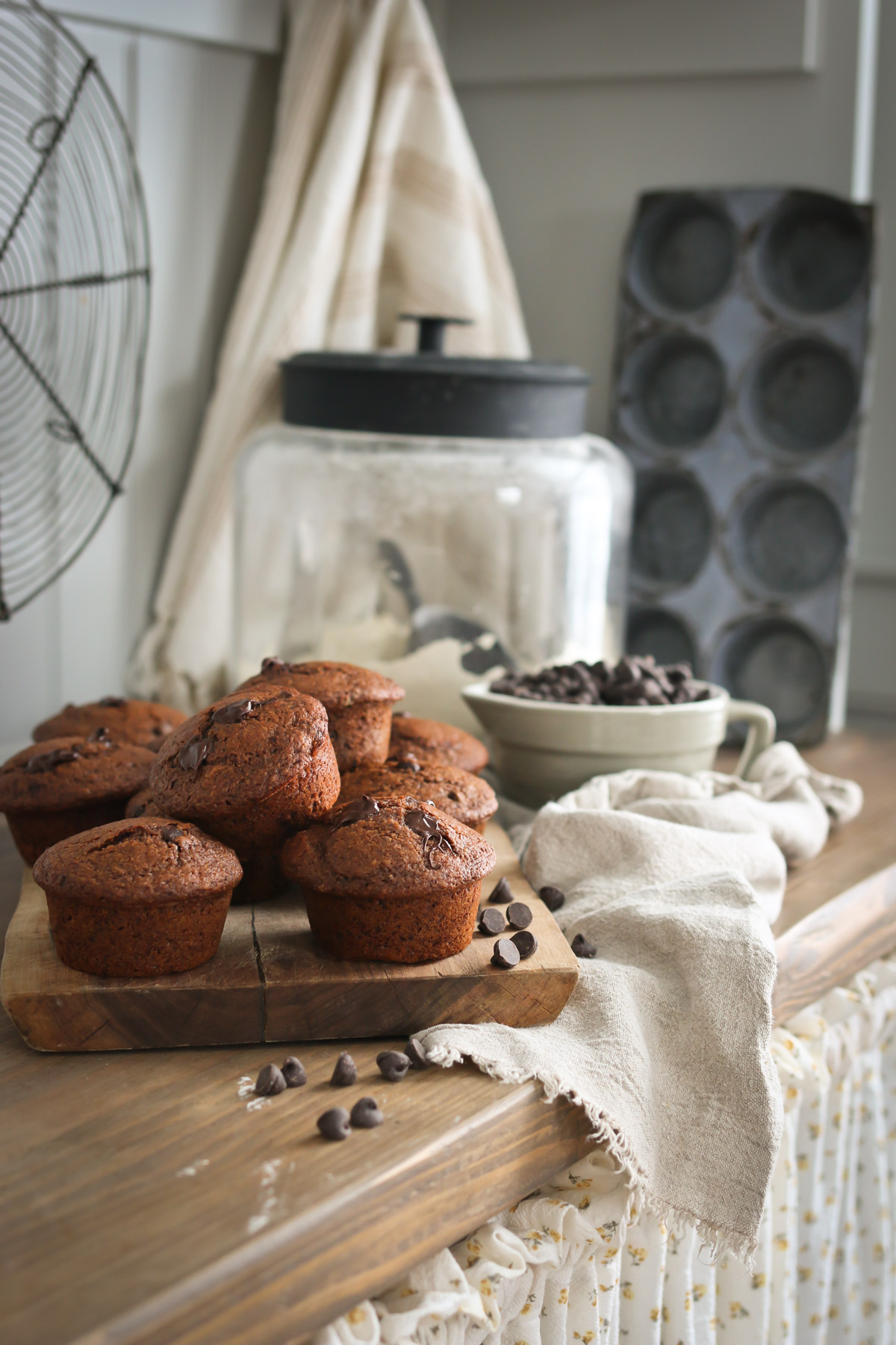 A pile of healthy chocolate muffins sits in a counter next to assorted baking supplies