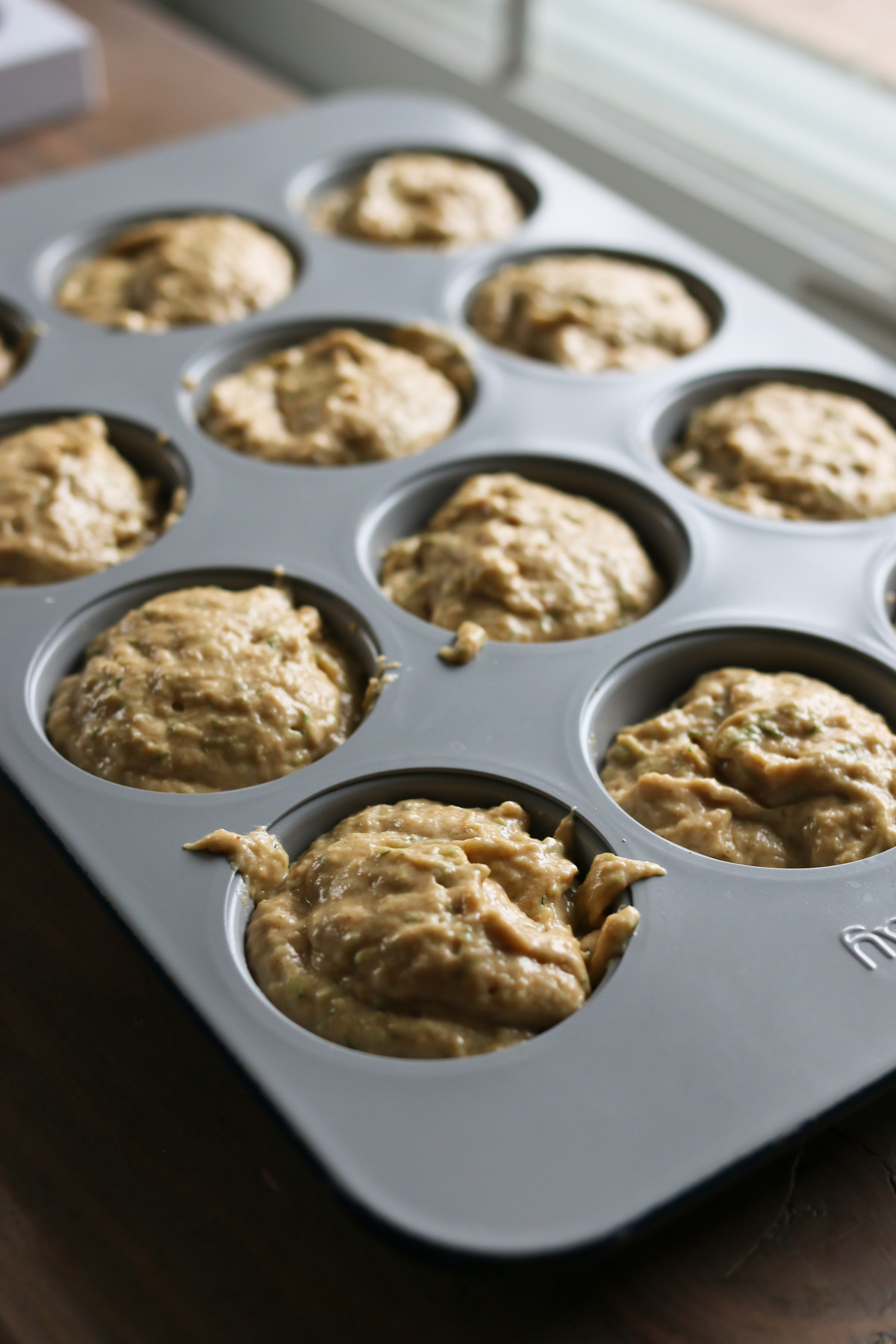 A muffin tin holds a batch of homemade whole wheat zucchini muffin batter