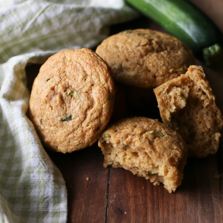 Whole wheat zucchini muffins are arranged next to a zucchini on a wooden cutting board