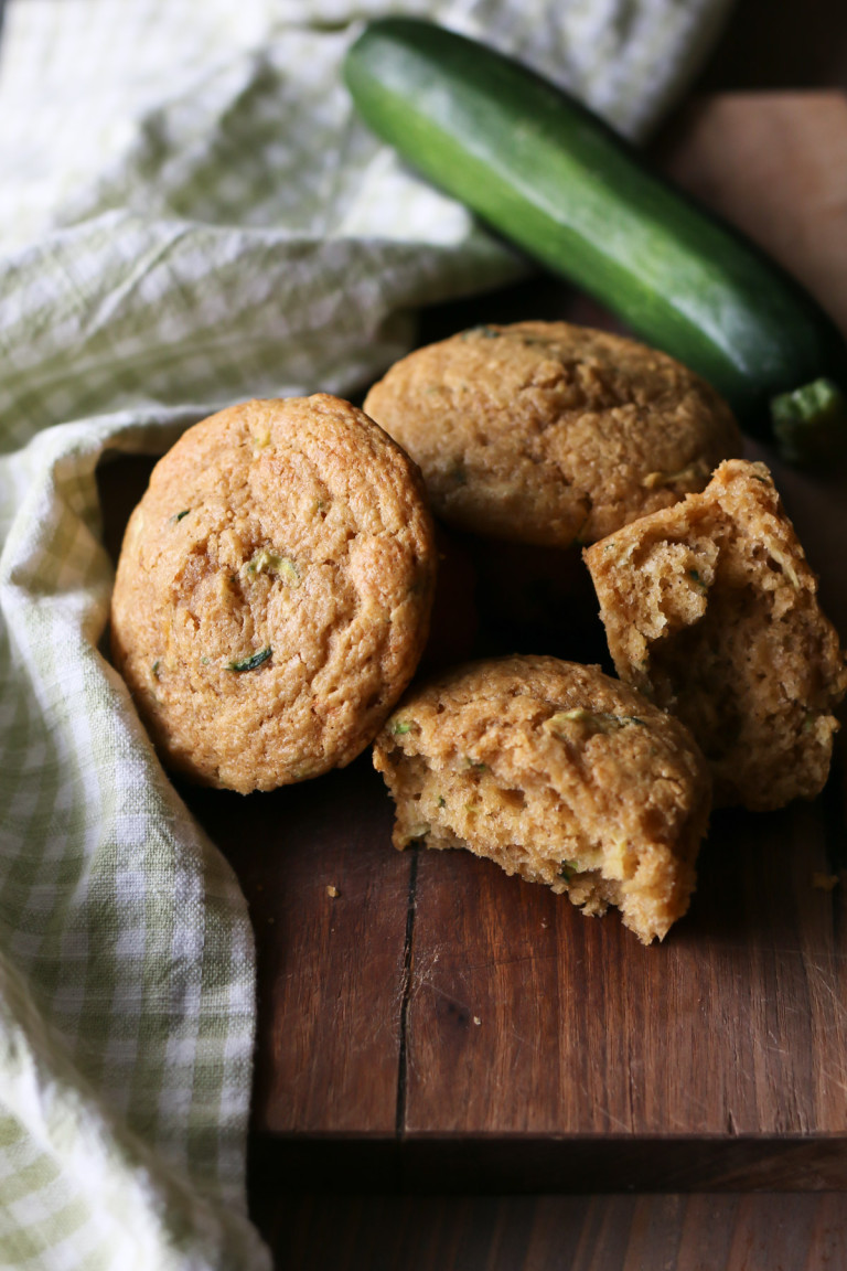 Whole wheat zucchini muffins are arranged next to a zucchini on a wooden cutting board