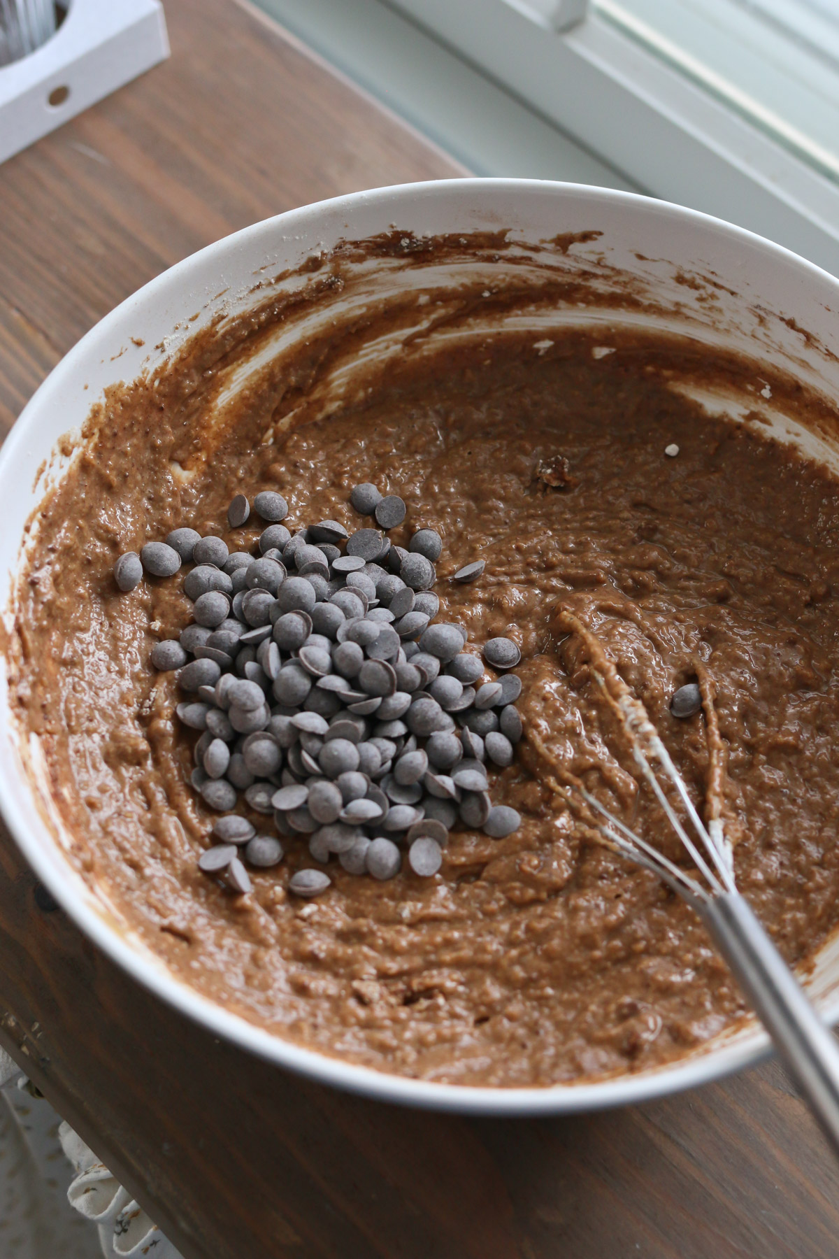 A bowl of chocolate muffin batter is sprinkled with chocolate chips before mixing