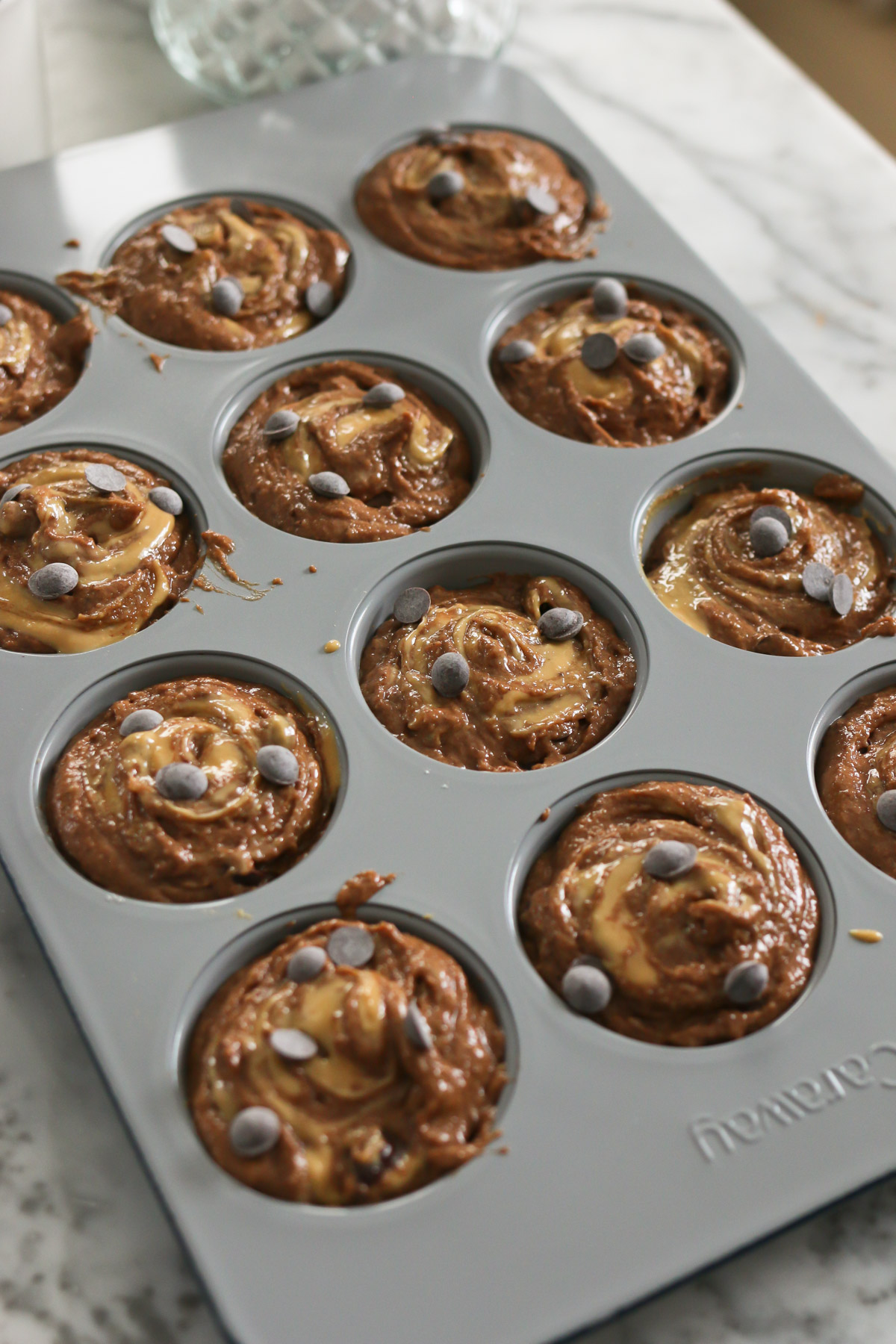 Muffin batter in a muffin tin is topped with chocolate chips